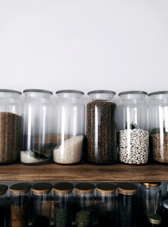 Neatly arranged glass jars filled with various grains and spices on a wooden shelf.